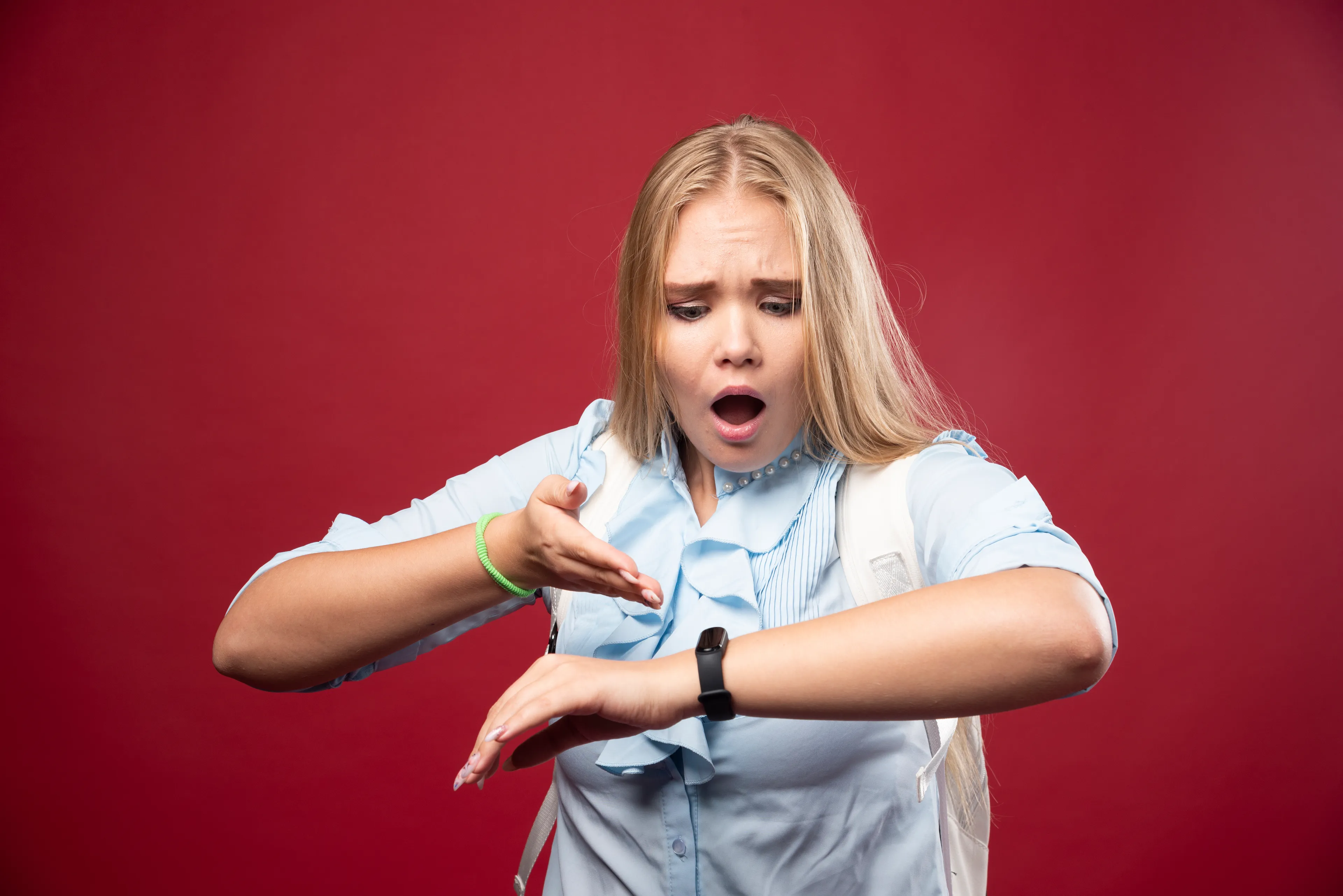 A shocked young woman with long blonde hair checks her watch, realizing she's late. How do you apologize?