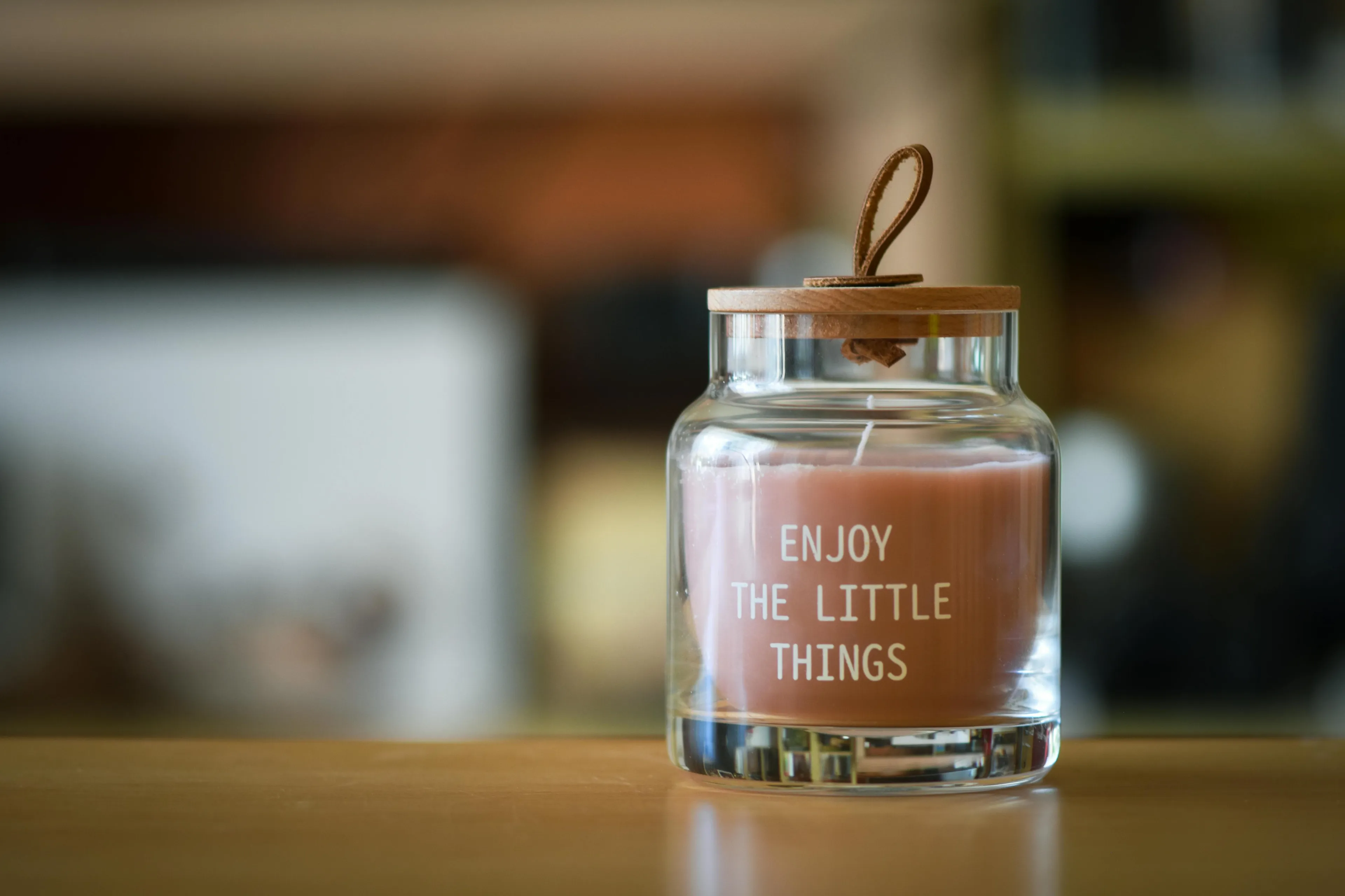 A thoughtful housewarming gift: a candle in a clear jar with a wooden lid, inscribed with "ENJOY THE LITTLE THINGS."