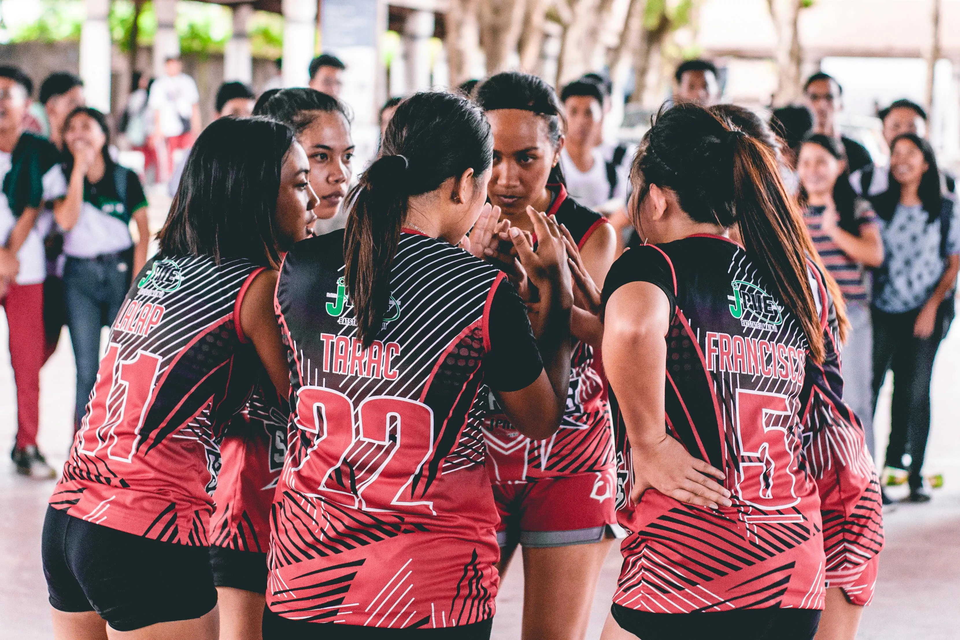 A close-up of a female sports team in red and black jerseys huddling, likely discussing strategies. Reaction to Rejection Quiz.
