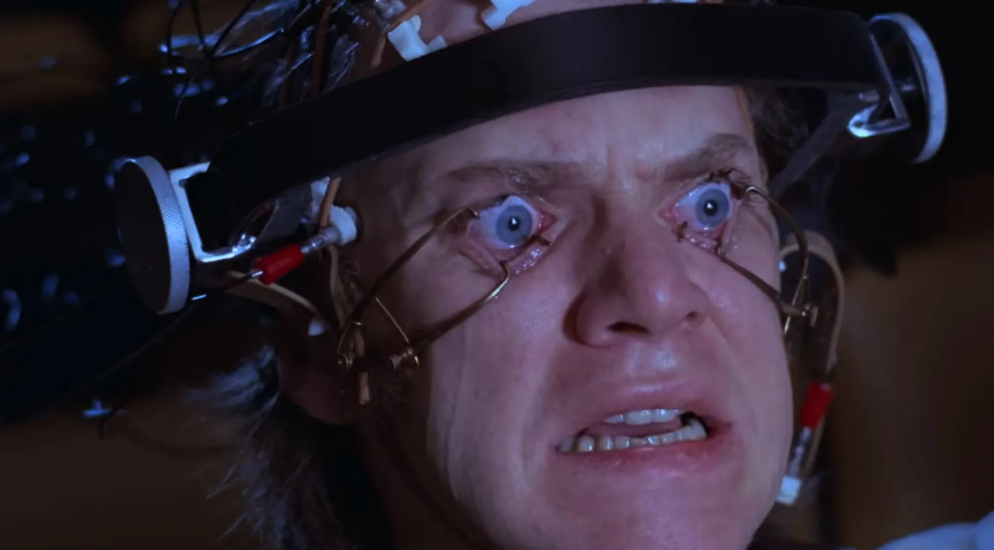 Close-up of a man's face with his eyes held open by devices, part of a disturbing movie scene quiz.