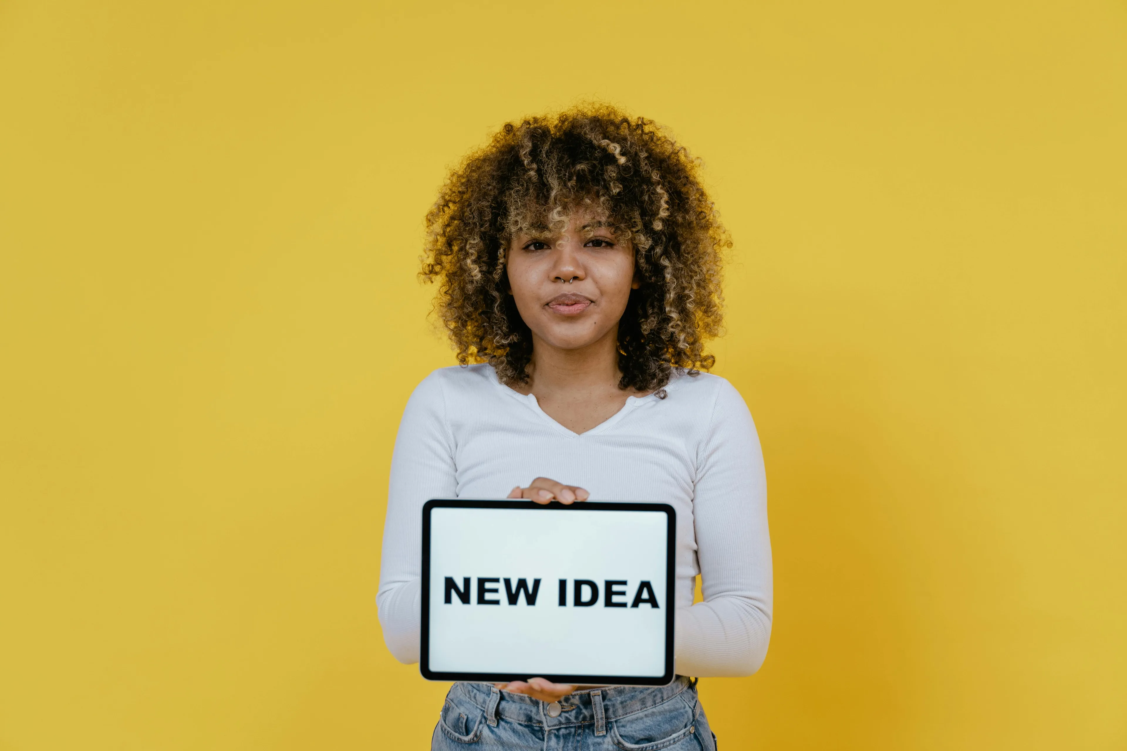 Young woman with curly hair holding a tablet displaying "NEW IDEA," reflecting reactions to rejection.