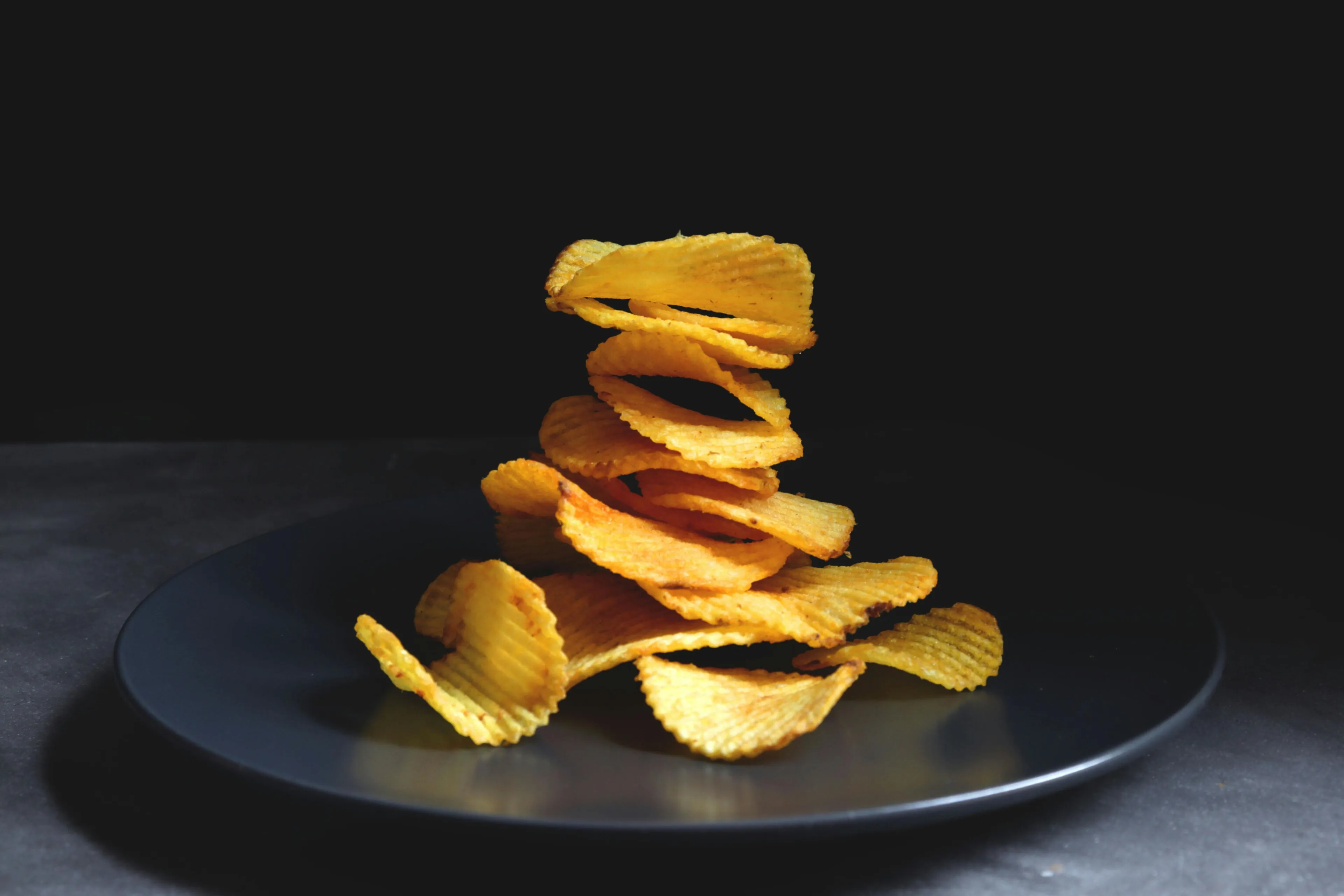 Golden, ridged chips stacked on a dark plate, a comforting snack.