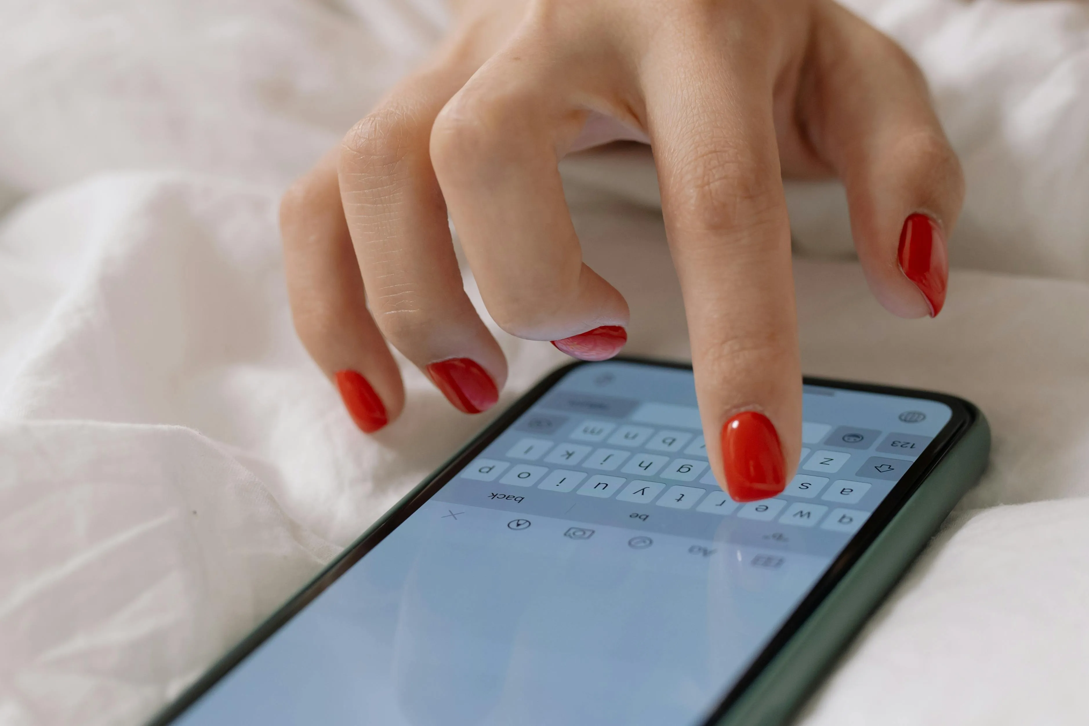 A hand with red nail polish typing on a smartphone, on a white background, suggesting a Reaction To Rejection.