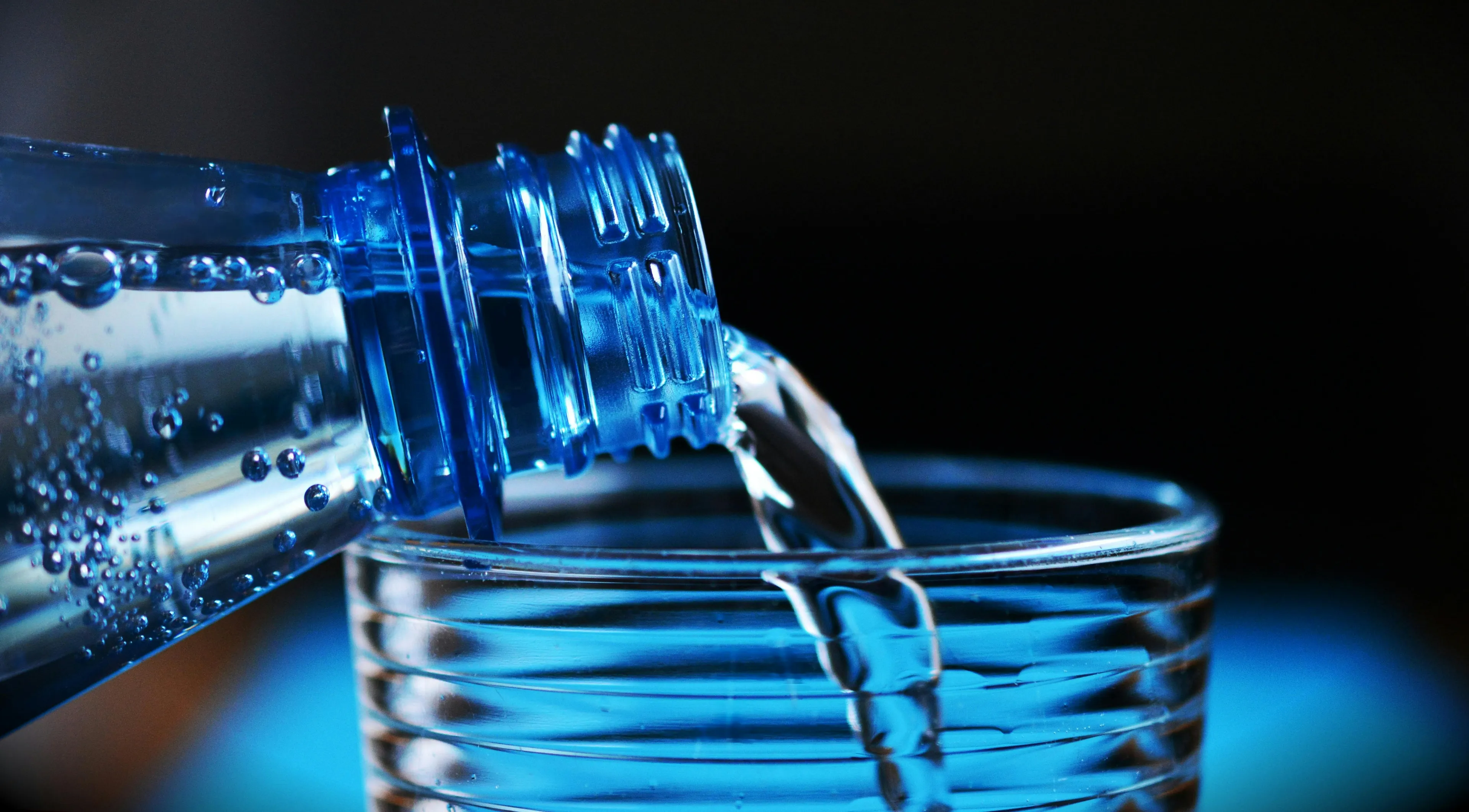 A blue plastic bottle pours sparkling water into a glass, highlighting bubbles and the refreshing recovery drink.