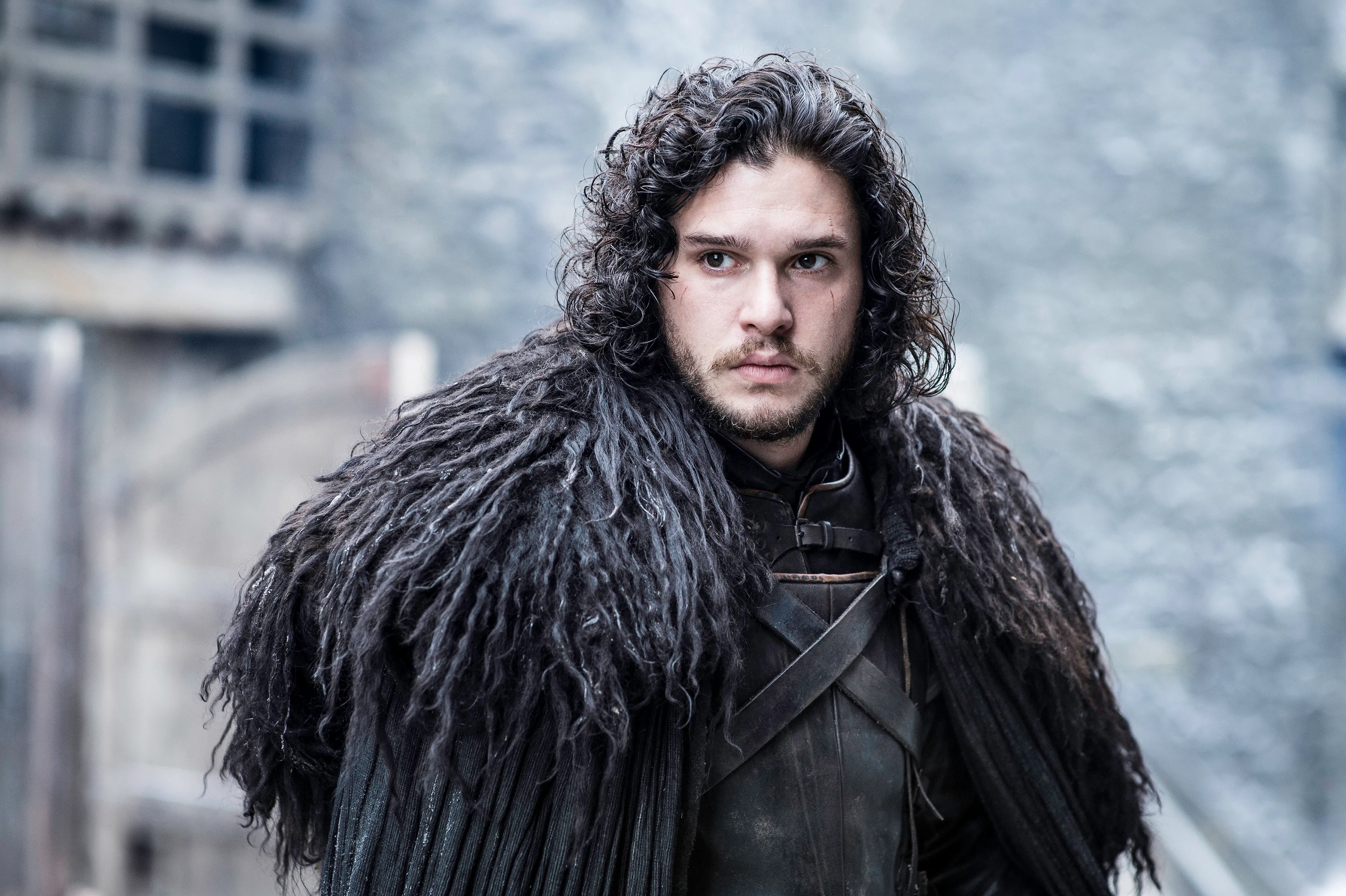 A determined Jon Snow with dark curly hair and beard, wearing a heavy, dark fur cloak and leather armor.
