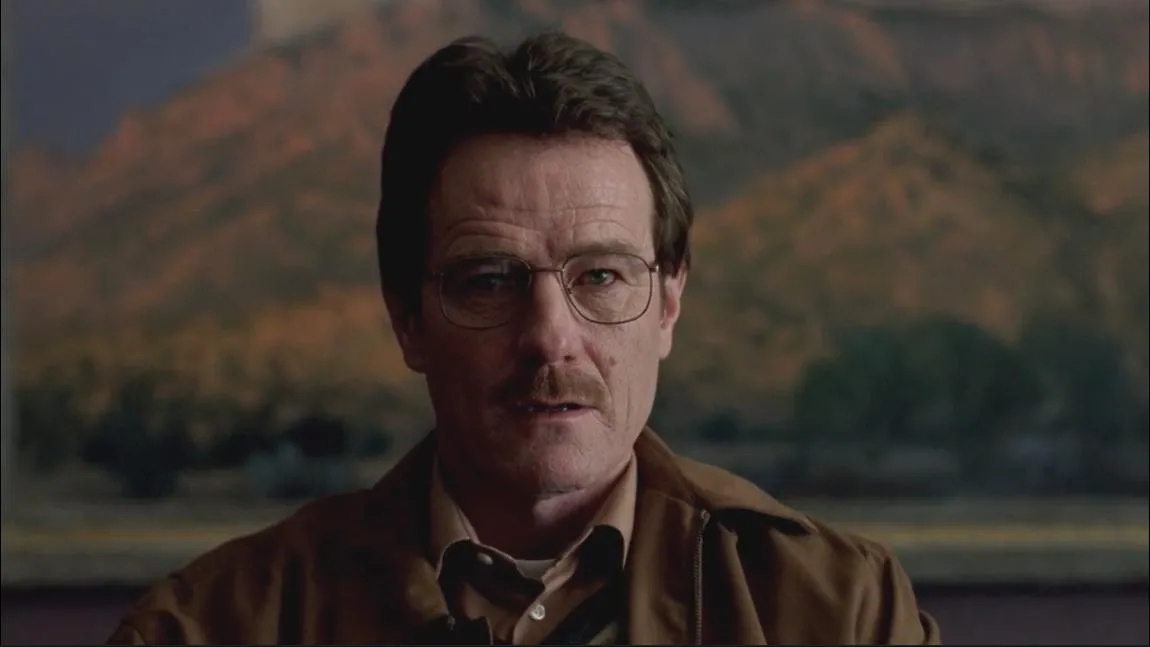 Walter White, wearing glasses and a brown jacket, stares intensely with a mountain landscape in the blurred background.