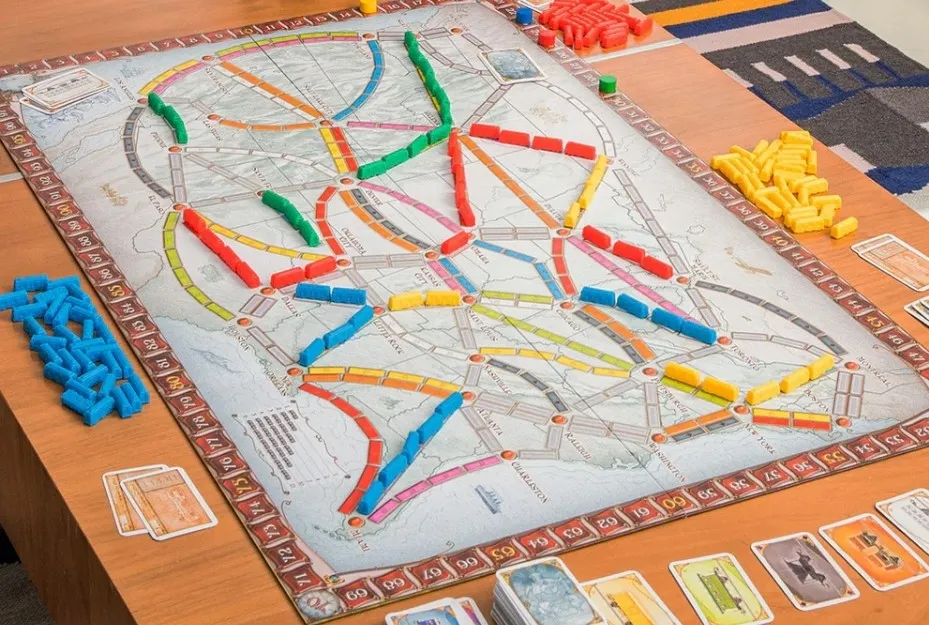 A board game of Ticket To Ride set up on a wooden table, with colorful train pieces and cards laid out.
