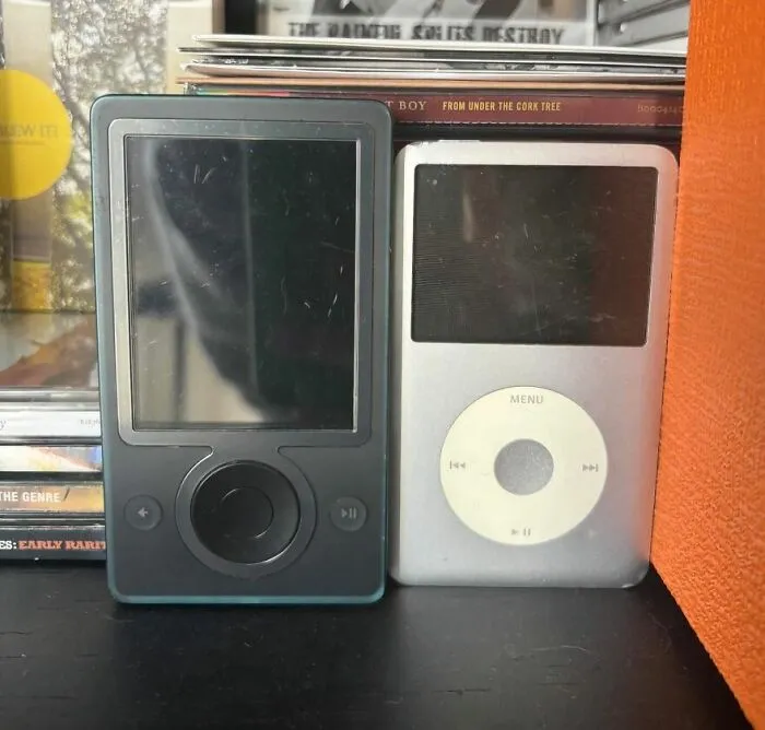 Two old MP3 players, a black Zune and a silver iPod, evoking a trip down memory lane for tech enthusiasts.
