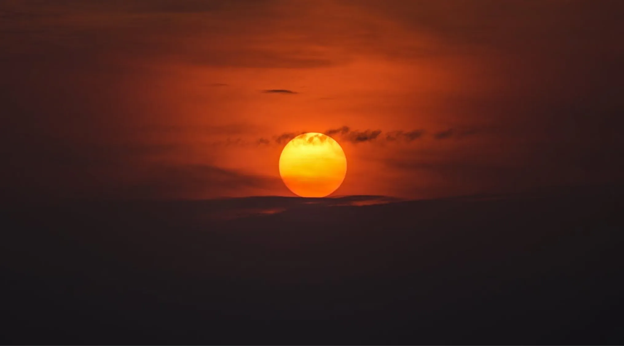 General Knowledge image showing the sun dipping below a dark horizon, vibrant orange and yellow against a cloudy sky.