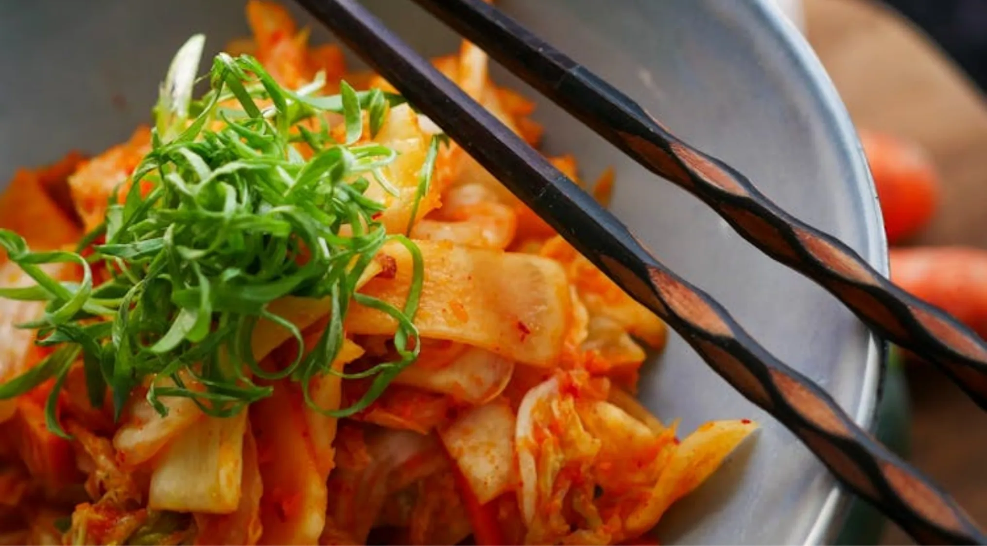 Close-up of vibrant kimchi with fresh green onions and chopsticks in a bowl, a general knowledge question about Korean food.