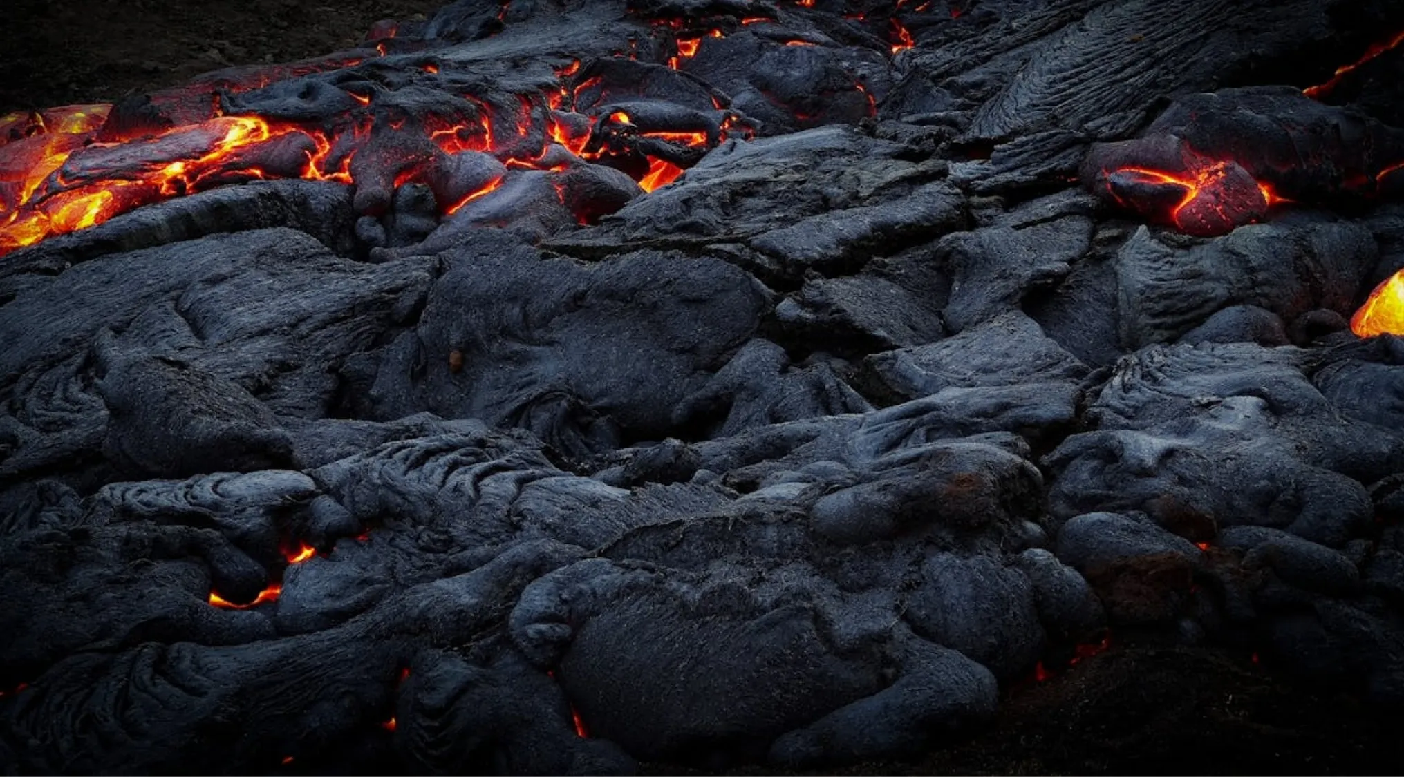 Dark, hardened General Knowledge rock with glowing orange molten rock visible underneath, flowing from a volcanic eruption.
