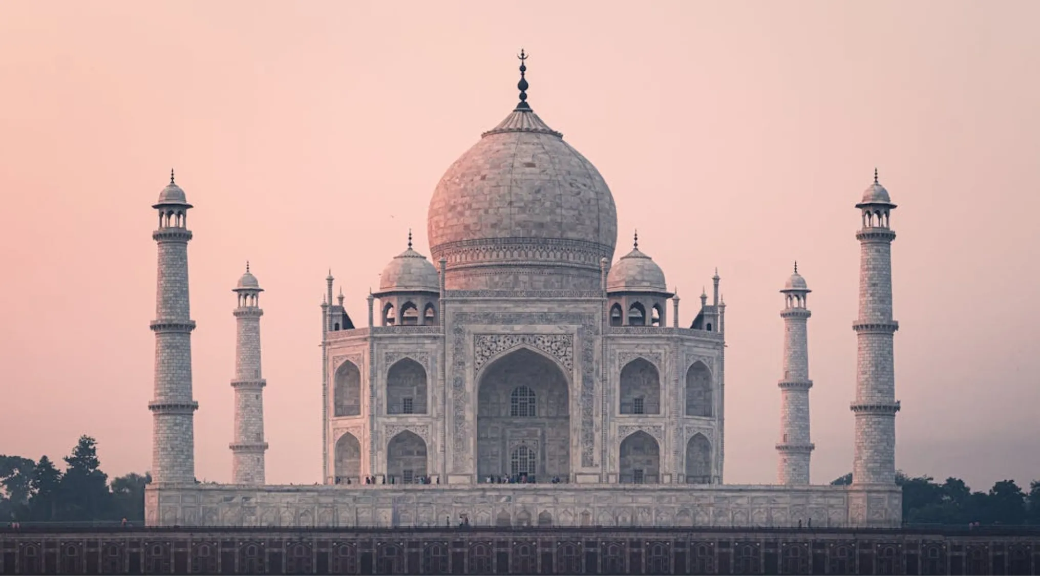 The Taj Mahal at sunset, its iconic marble structure glowing under a soft pink sky, a general knowledge landmark.