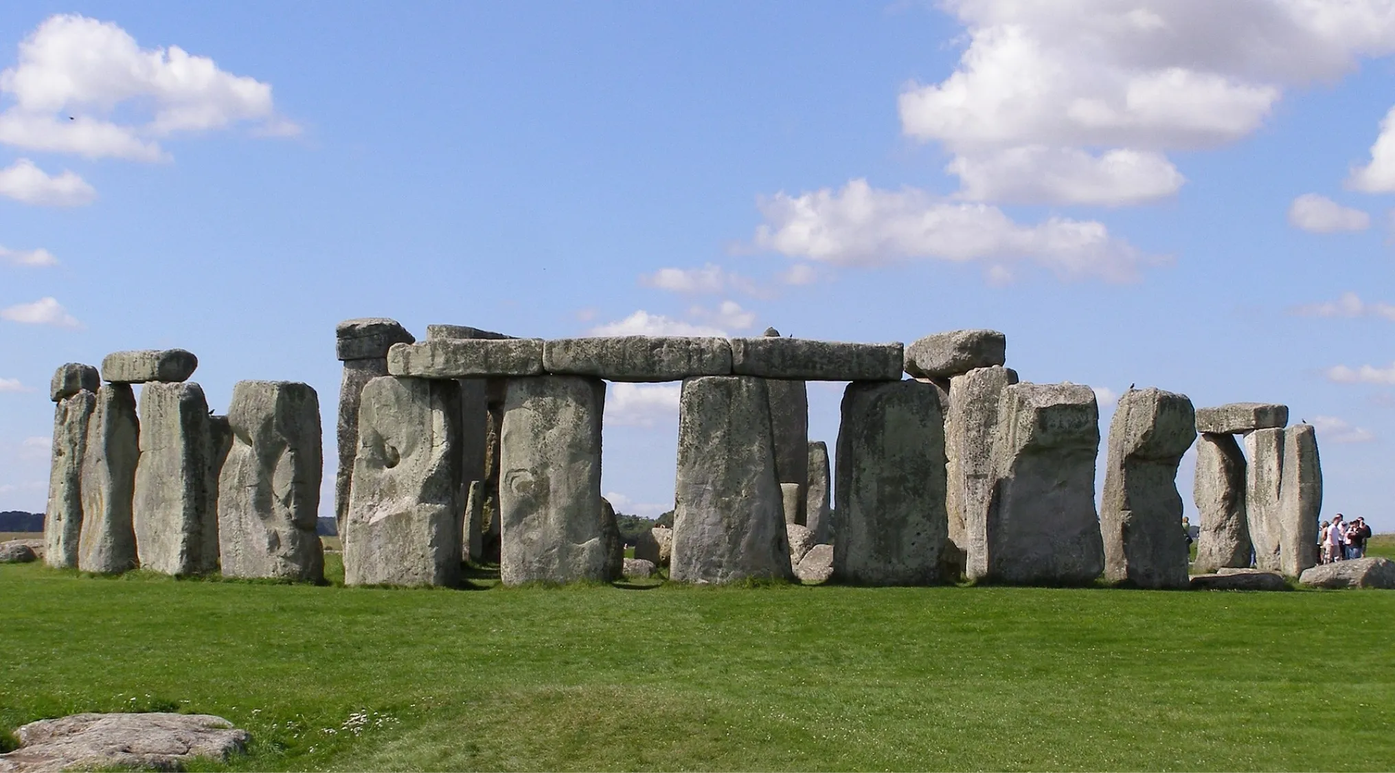 Stonehenge, a historic landmark and ancient monument. Towering sarsen stones on green grass under a blue sky with clouds. General Knowledge.