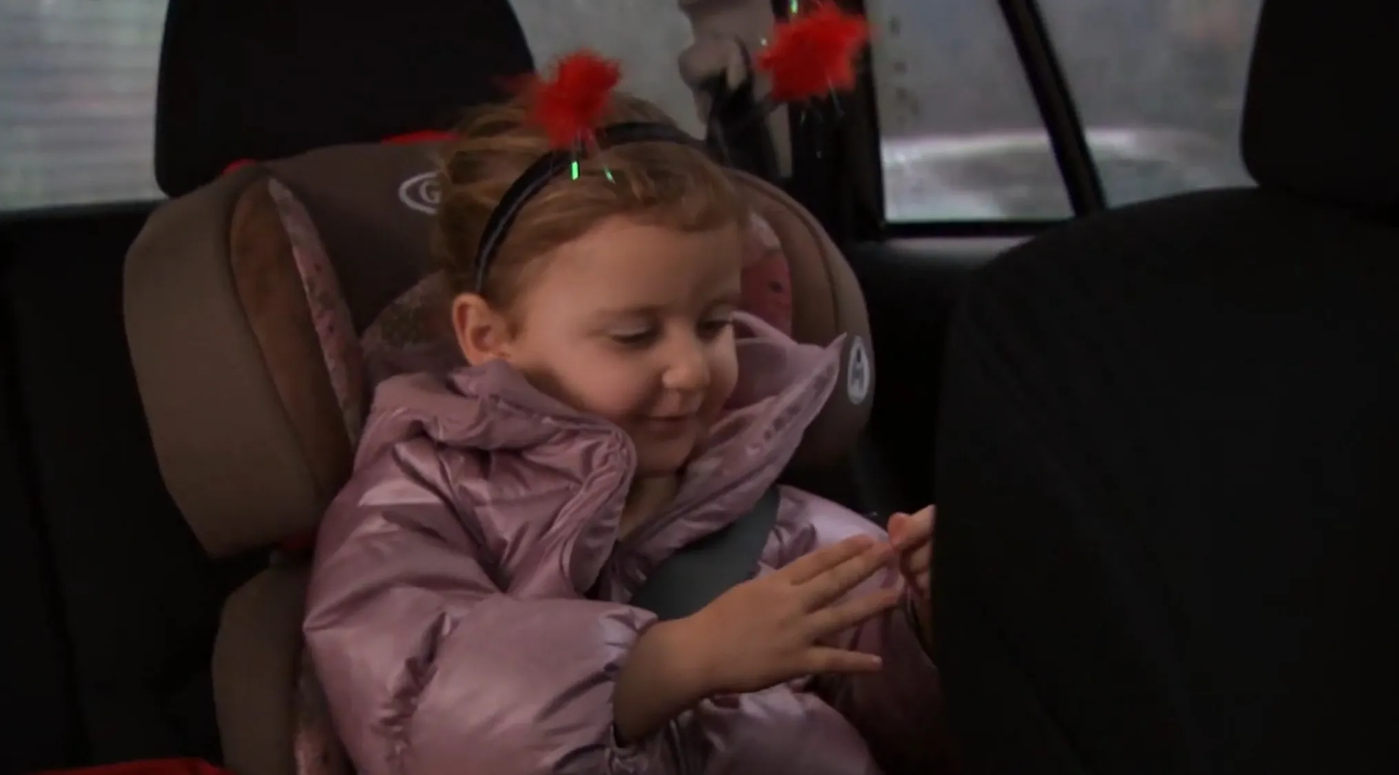 A young girl, likely Jim and Pam's first child, sits in a car seat wearing a pink jacket and festive headband. The Office Quiz.