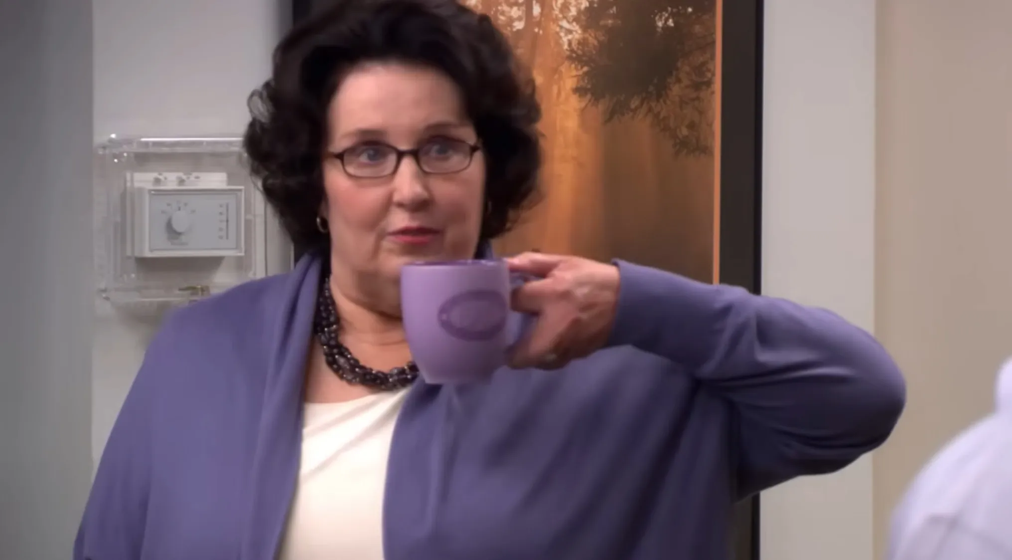 Phyllis from The Office, wearing glasses and a purple cardigan, holding a matching mug. Take this Office Quiz!