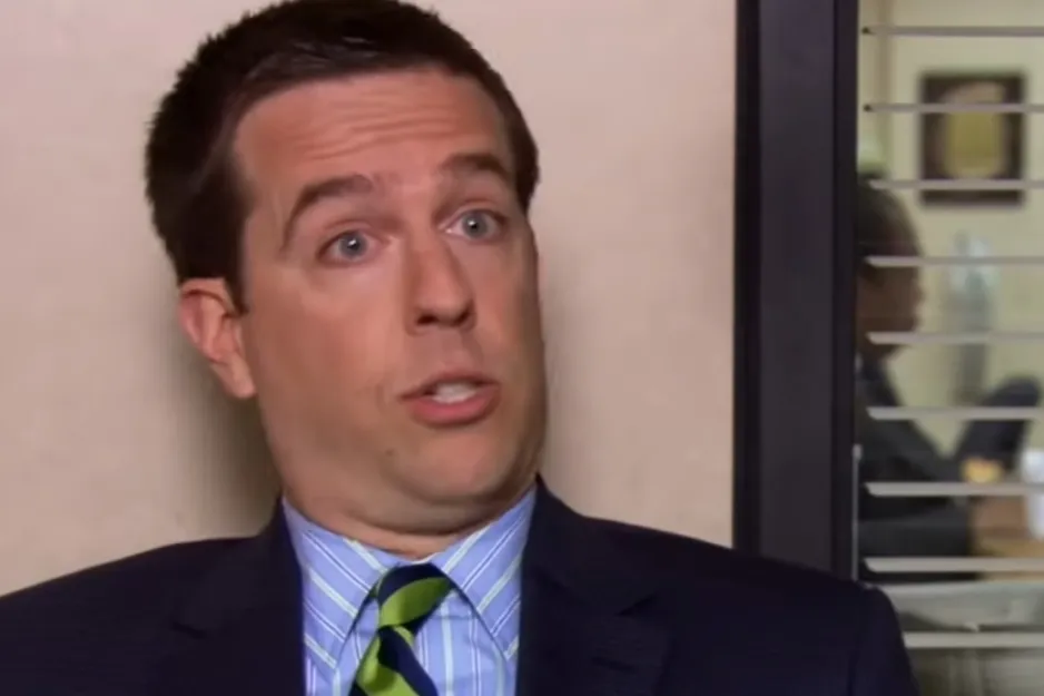 Andy Bernard, from The Office, looks surprised, wearing a suit and striped tie, discussing foster care.
