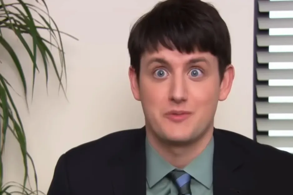 Gabe from The Office looking shocked with wide blue eyes, wearing a suit and tie. He might have grown up in foster care.