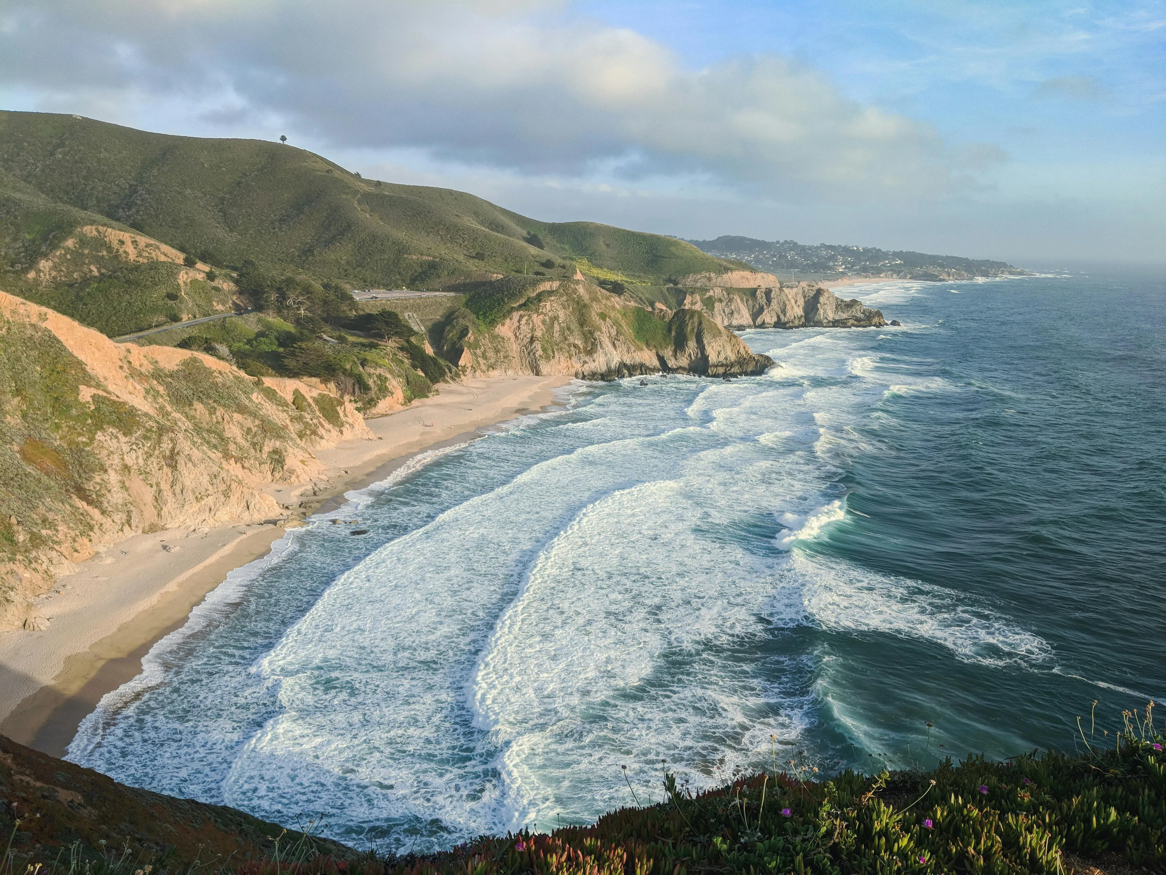 Waves crashing on a sandy beach below cliffs and green hills, illustrating General Knowledge. The largest ocean on Earth.