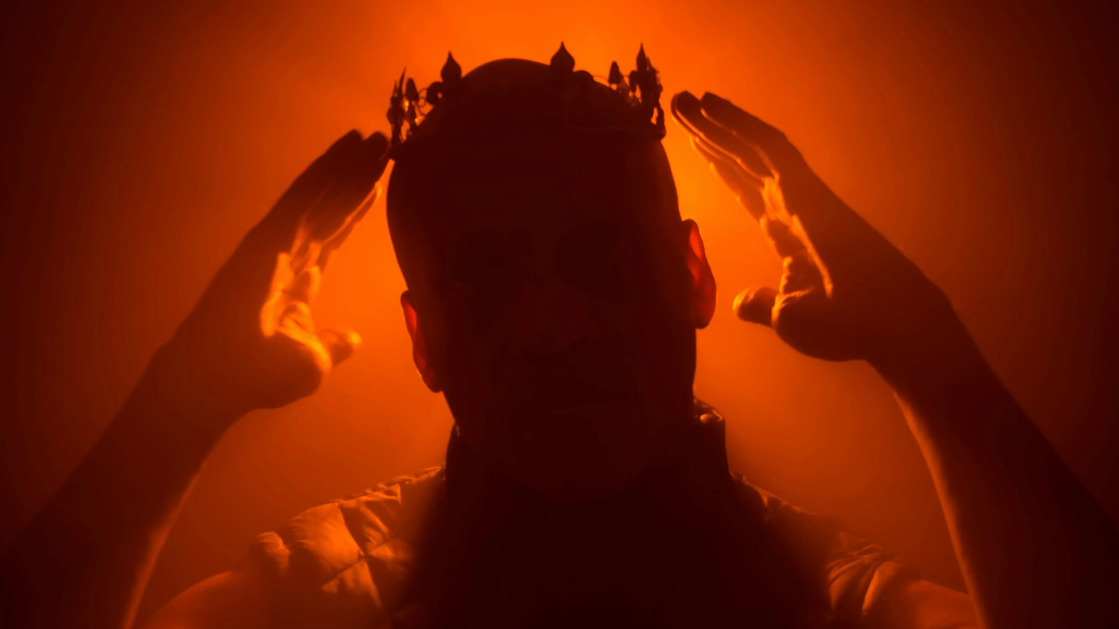 A shadowed person wearing a crown in an orange glow, hands raised, exploring General Knowledge. Who wrote Hamlet?