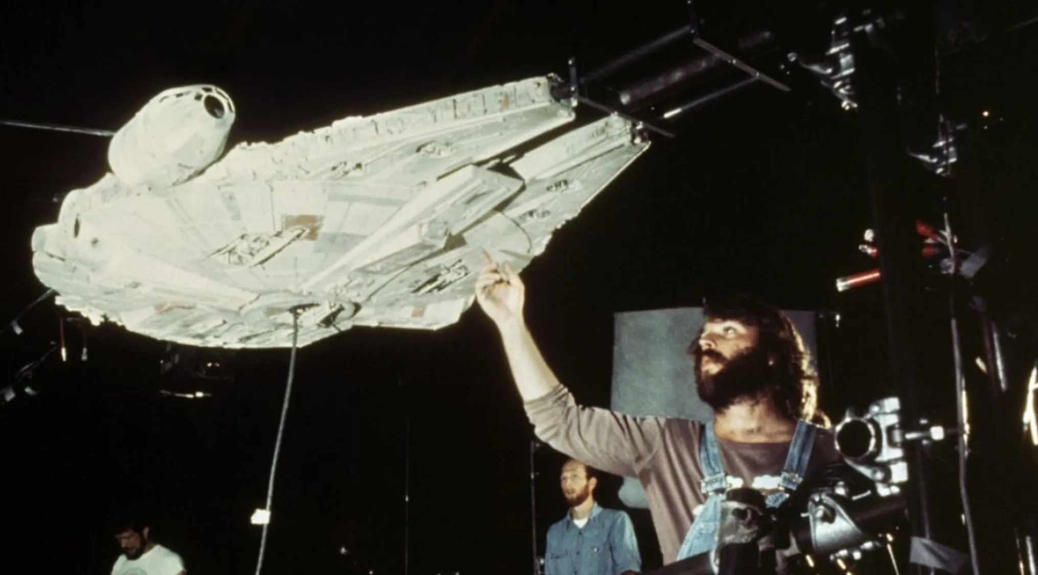 Behind the scenes of a movie franchise, a crew member adjusts a large model of a spaceship, hinting at Star Wars.