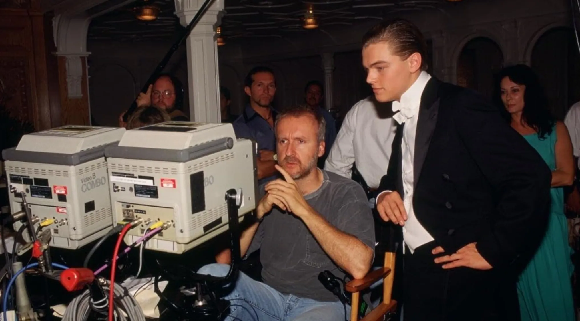 BTS image of the Titanic set. Director James Cameron watches monitors as Leonardo DiCaprio stands by, recognizing the film.