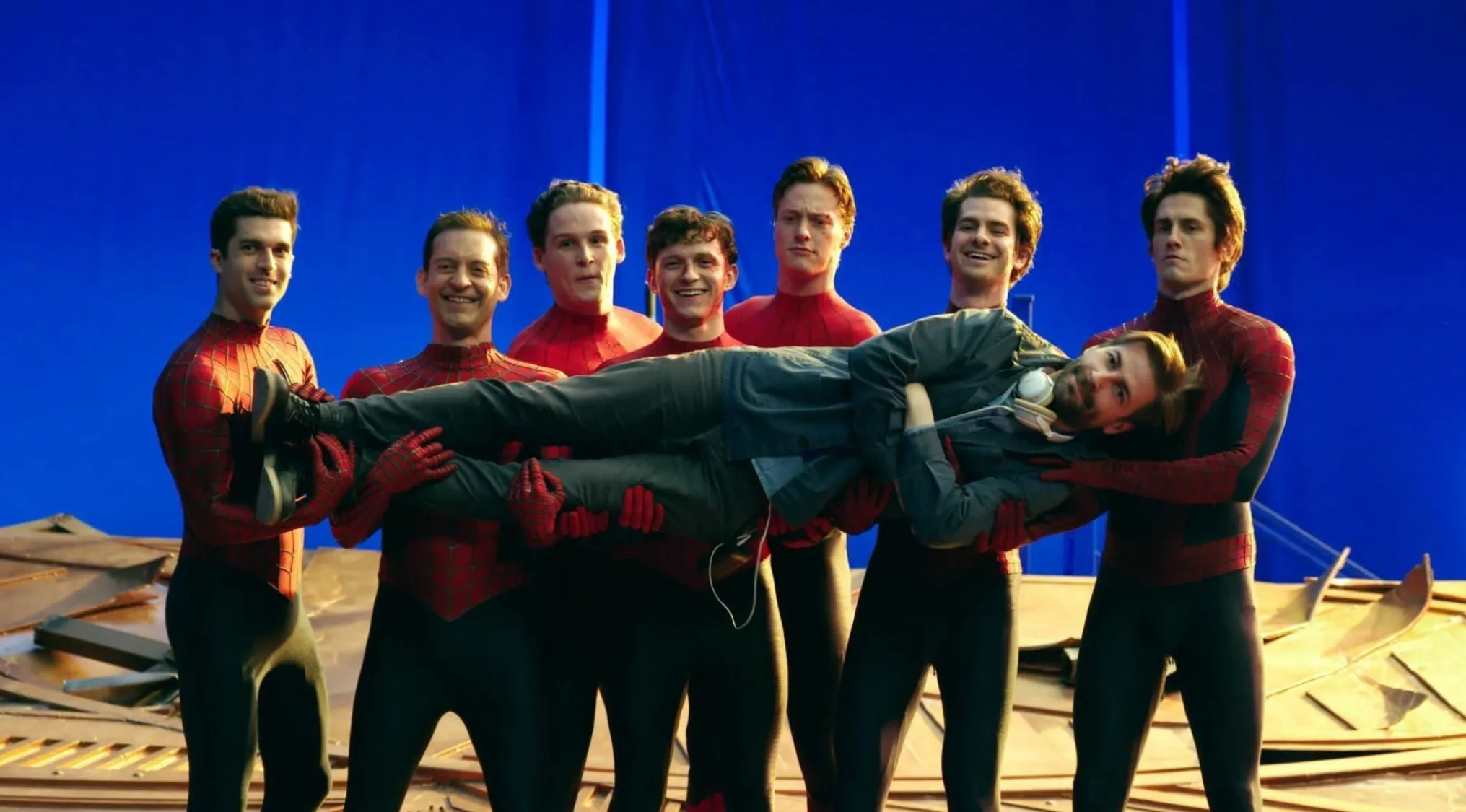 BTS image: Seven men in Spider-Man suits on a blue screen set, carrying another man. Guess the movie.