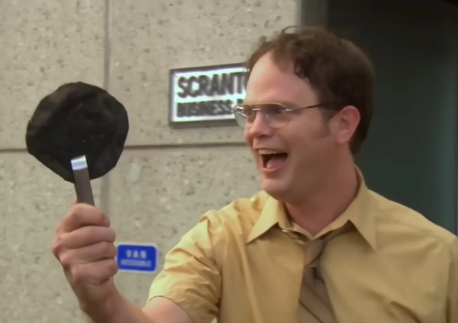 Dwight Schrute, holds up a burnt pita, laughing after the Dunder Mifflin evacuation.