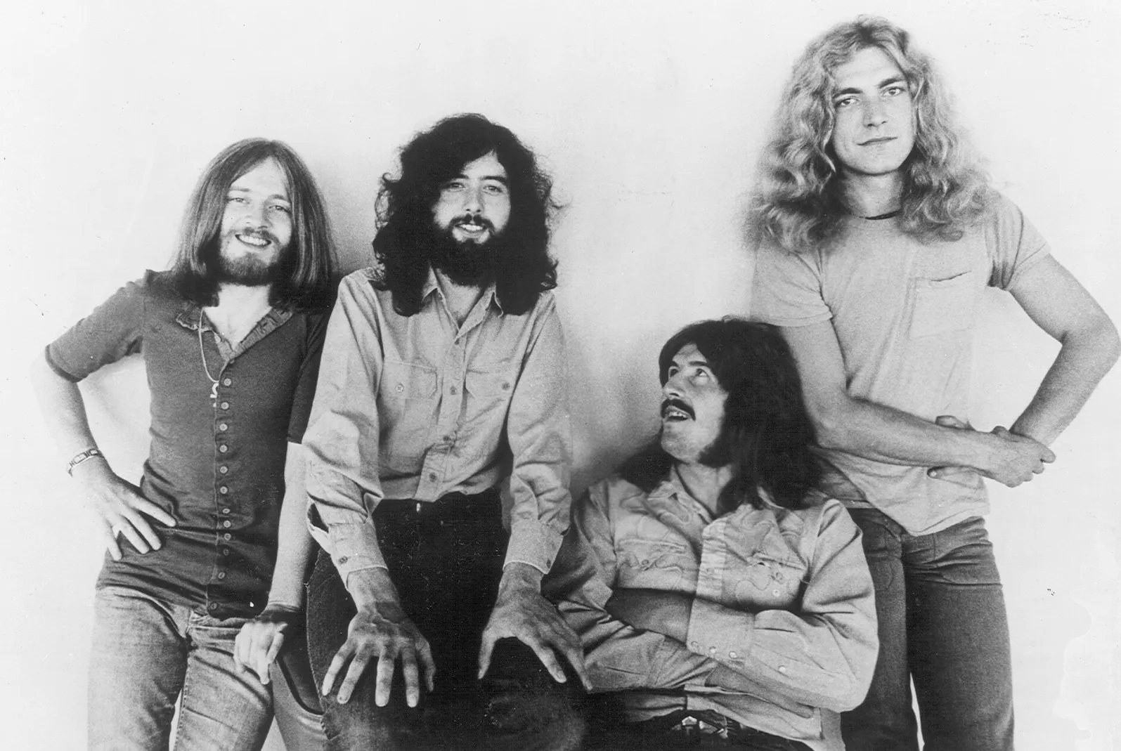 Black and white photo of Led Zeppelin, four members with long hair and beards, posing casually.