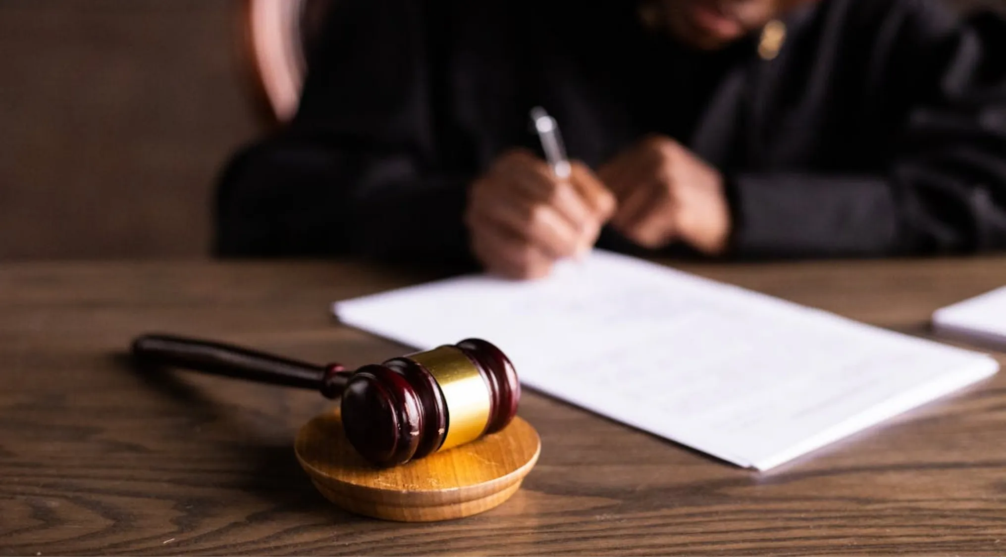 A gavel rests on a wooden desk with a person blurred in the background writing on a document. Focus on Australian Citizenship and the role of courts in Australia.