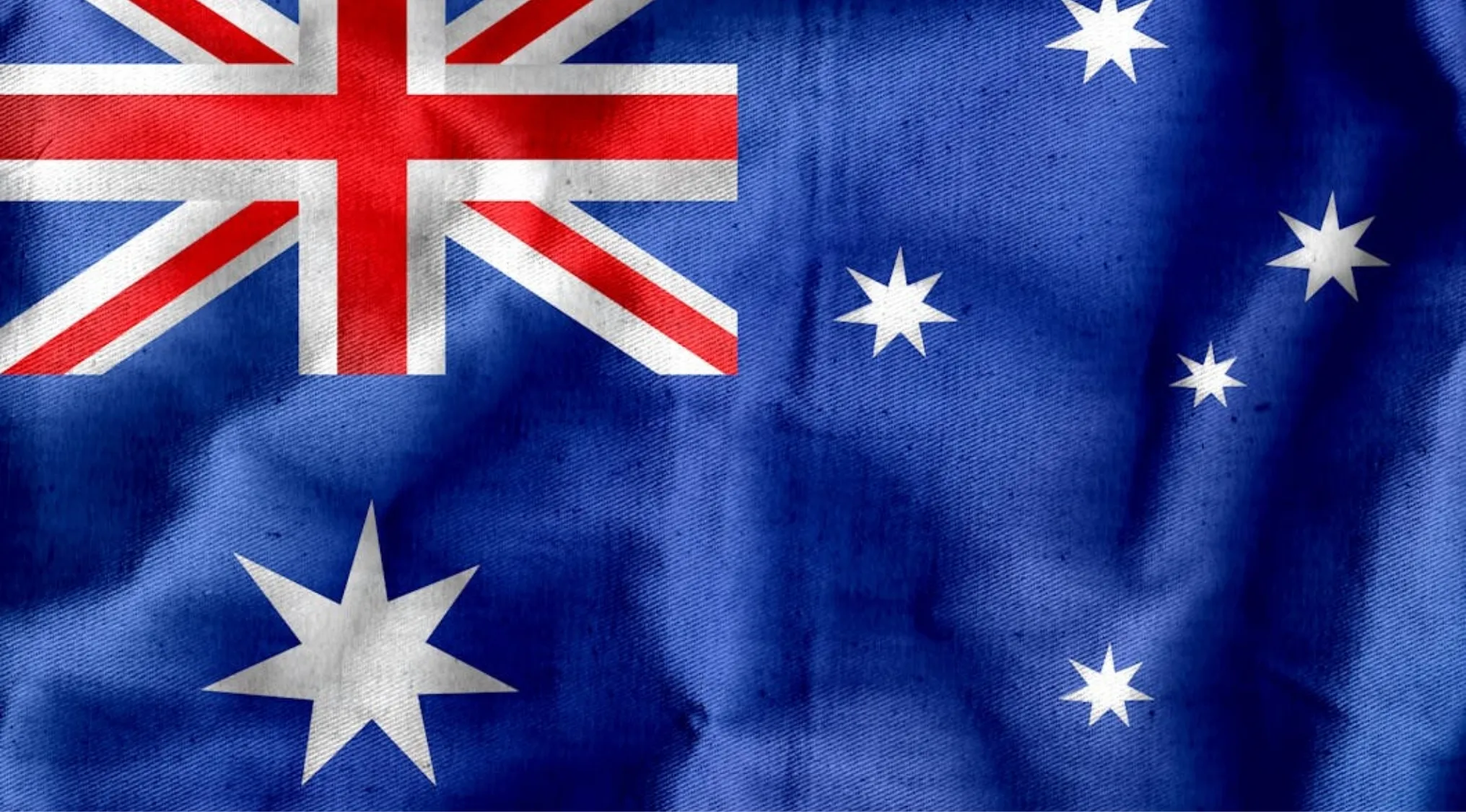 The Australian National Flag, featuring the Commonwealth Star and Union Jack, rippling with a textured fabric effect.