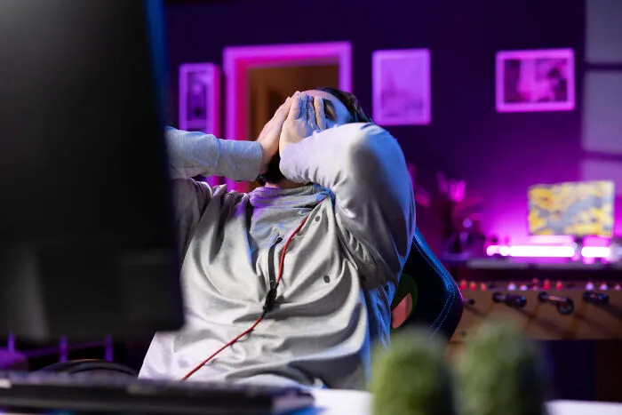 Man in a gray hoodie showing frustration in a colorful room, highlighting moments of betrayal from being a good person.