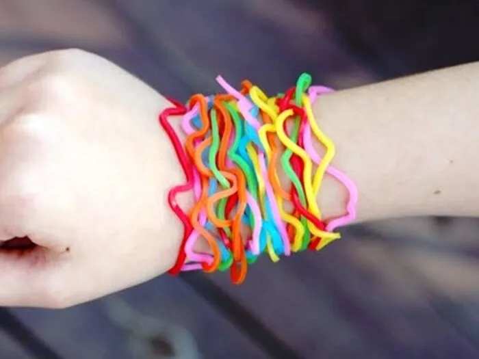 A person's wrist adorned with numerous colorful rubber band bracelets, reminiscent of childhood fun and taking a trip down memory lane.