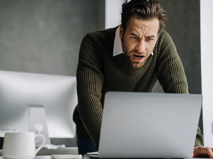 Man in a green sweater leaning over a laptop, displaying frustration while working on customer service issues.