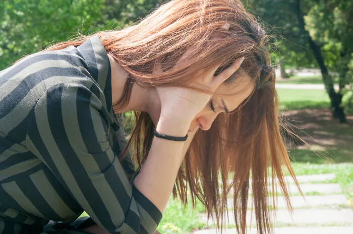 Young woman outdoors holding her head in distress, representing being a good person facing total betrayal and shock.