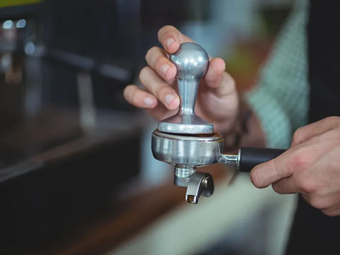 Barista tamping coffee grounds with tamper in portafilter, symbolizing rude customers learning not to mess with staff.