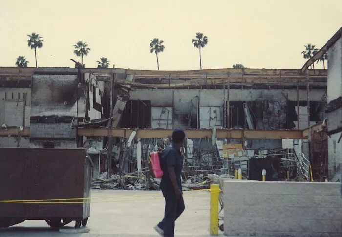 Person walking near a damaged building with palm trees, depicting what was happening in the year you were born.