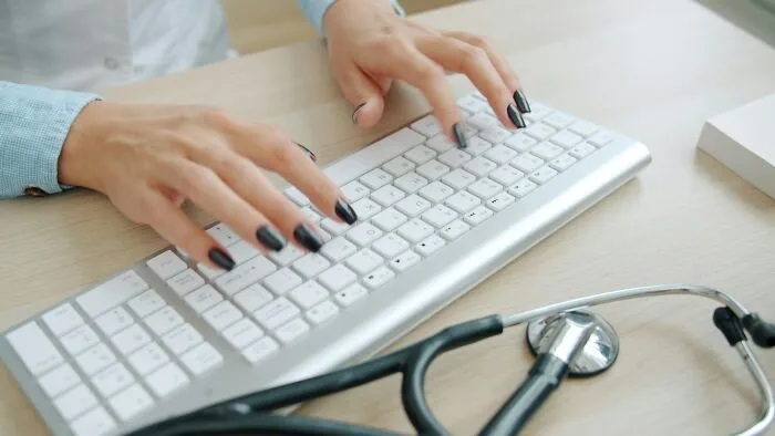 A medical professional types on a computer keyboard with a stethoscope nearby, highlighting patient care in emergencies.