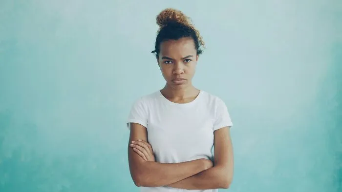 A serious young woman with a high bun, arms crossed, offering advice for dads raising daughters.