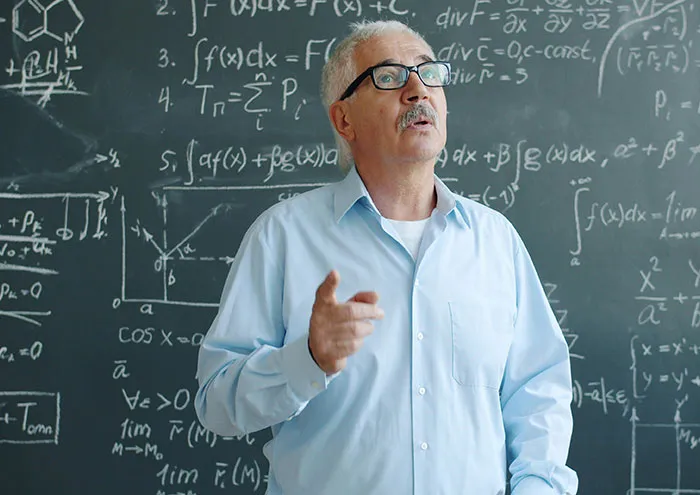 Older scientist with glasses explaining unproven scientific theories in front of a chalkboard filled with equations.