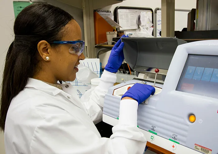 Scientist in lab coat and gloves operating a laboratory device while researching theories not yet proven.