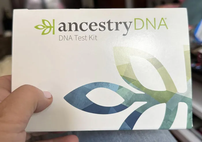 Hand holding an ancestry DNA test kit box, related to scientists' theories in genetics and ancestral research.