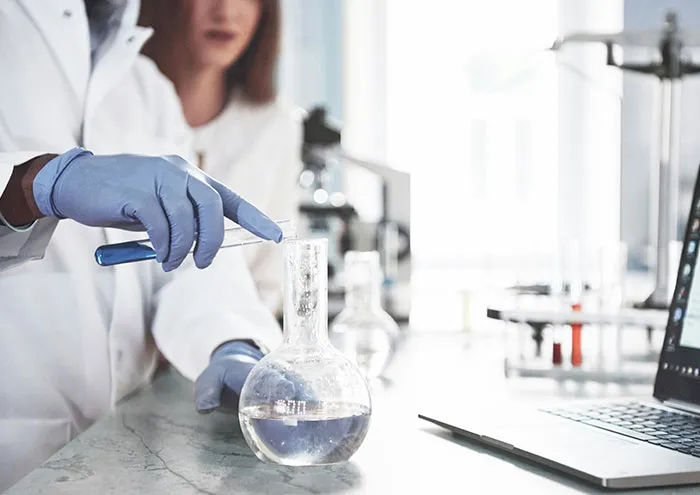 Scientist in lab coat conducting experiments with glassware and laptop, exploring unproven scientific theories.