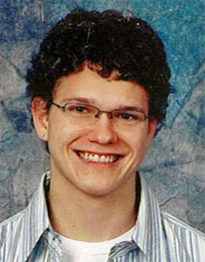 Young man with curly hair and glasses smiling, representing creepy and mysterious things that lose people sleep over.