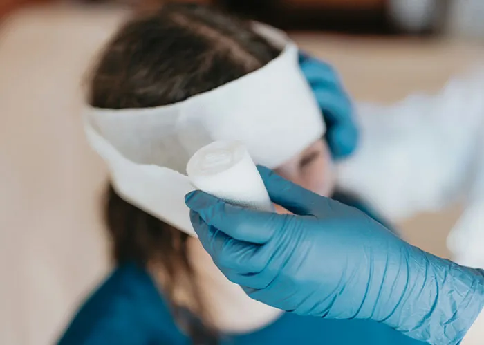 Person wearing a white bandage on head with a hand in blue gloves holding gauze, related to police chasing the wrong person.
