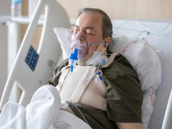 A patient in a hospital bed with an oxygen mask and chest brace, illustrating stories of patients being ignored in emergencies.