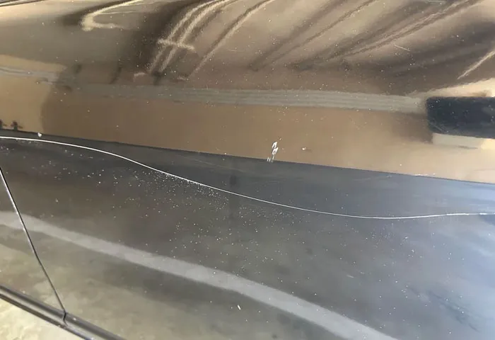 Close-up of a scratched black car door illustrating harmless but effective revenge on jerks with subtle damage.
