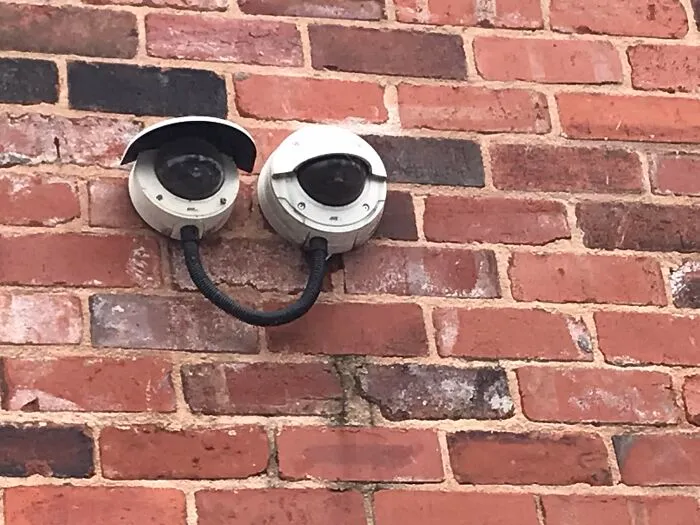 Two security cameras on a brick wall forming a smiling face, an example of pareidolia captured in a photo.
