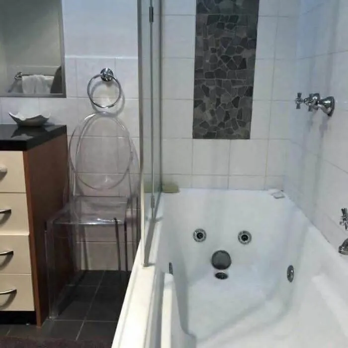 Bathroom with a bathtub and transparent chair creating a pareidolia effect resembling a face in the scene.