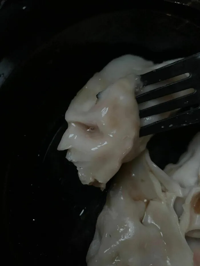 Fork holding dumpling resembling a human face, an example of pareidolia captured in a close-up food photo.
