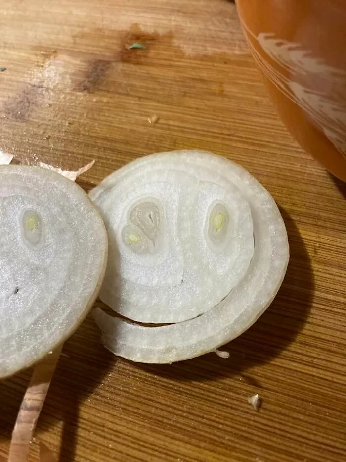 Onion slices on a wooden cutting board resembling a smiling face illustrating pareidolia in everyday objects.